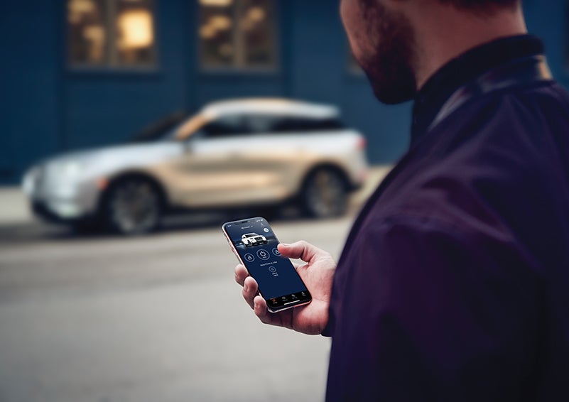 A person is shown interacting with a smartphone to connect to a Lincoln vehicle across the street. | Hooks Lincoln in Fort Worth TX