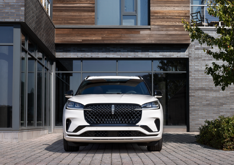 A white 2025 Lincoln Aviator® SUV is shown parked outside a modern building with gray brick and wood accents. | Hooks Lincoln in Fort Worth TX