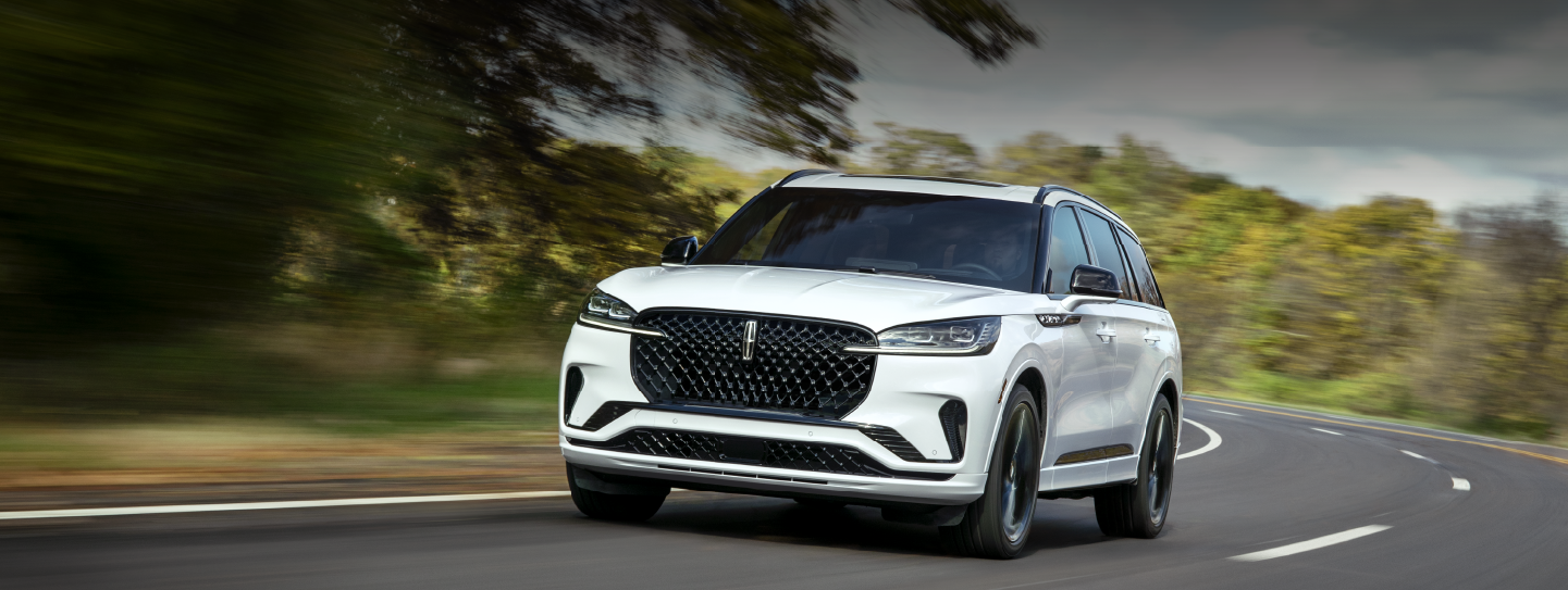 A white 2025 Lincoln Aviator® SUV is being driven down a road lined with trees. | Hooks Lincoln in Fort Worth TX