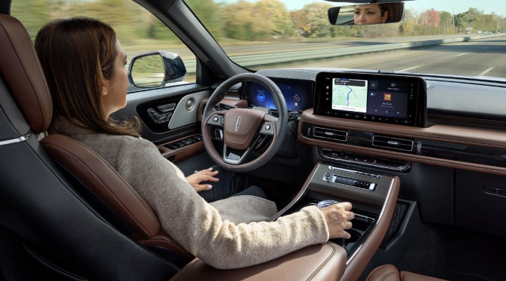 A 2026 Lincoln Aviator® SUV is being driven hands-free on a highway near a forest | Hooks Lincoln in Fort Worth TX