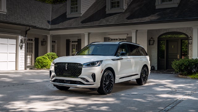 A white 2026 Lincoln Aviator® SUV is parked in the driveway of a luxury home. | Hooks Lincoln in Fort Worth TX