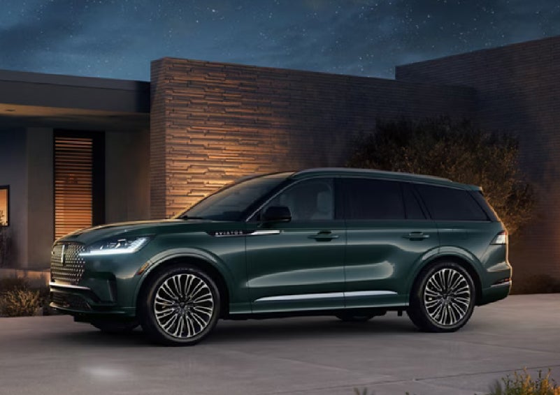 A green 2027 Lincoln Aviator® SUV is parked outside a contemporary home. | Hooks Lincoln in Fort Worth TX