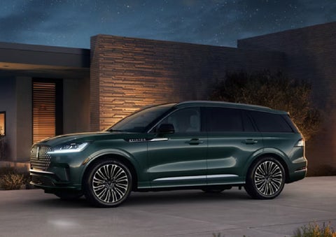 A green 2027 Lincoln Aviator® SUV is parked outside a contemporary home. | Hooks Lincoln in Fort Worth TX
