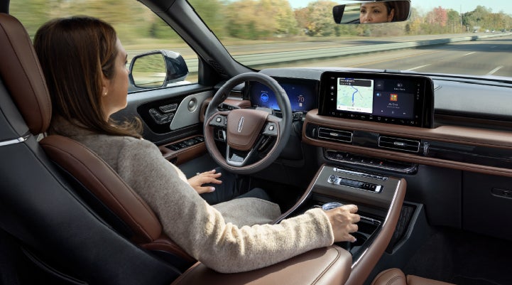 A 2027 Lincoln Aviator® SUV is being driven hands-free on a highway lined with trees. | Hooks Lincoln in Fort Worth TX