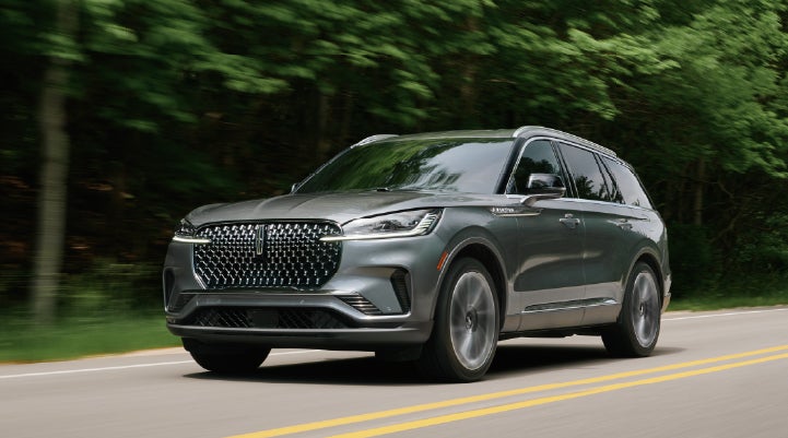 A 2027 Lincoln Aviator® SUV is being driven down a road lined with trees. | Hooks Lincoln in Fort Worth TX