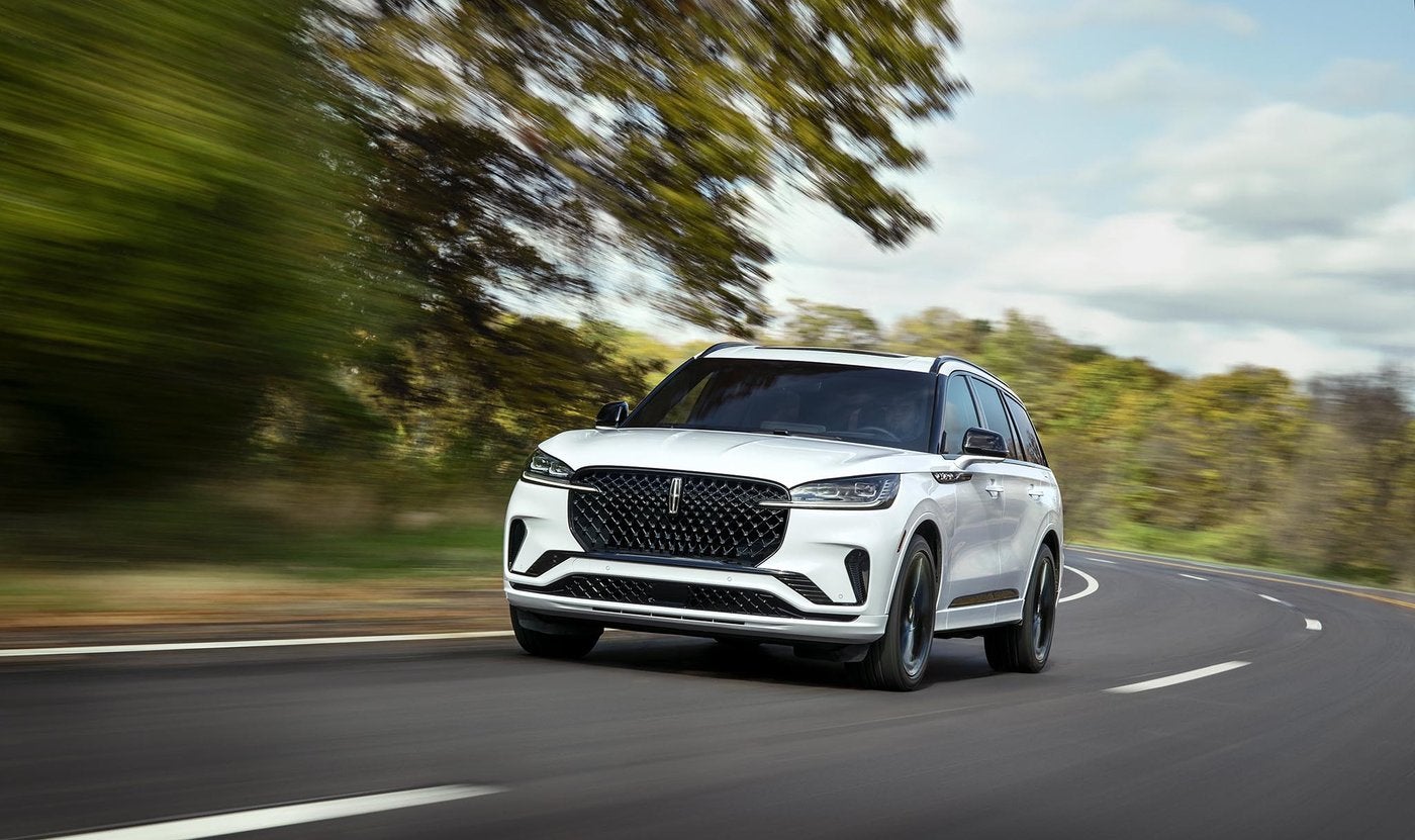 White 2026 Lincoln Aviator driving on a tree lined road for Fort Worth TX owners